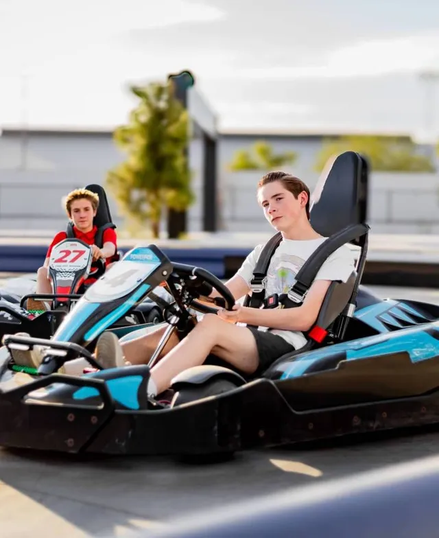 Two people driving black-and-blue go-karts on an outdoor track.