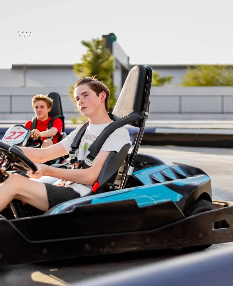 Two go-kart racers on an outdoor track, with a driver in a black-and-blue kart in the foreground