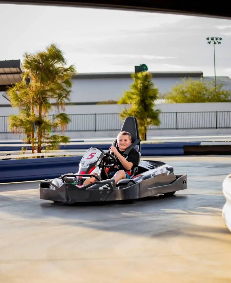Person driving a black go-kart on an outdoor track, wearing a helmet and smiling.