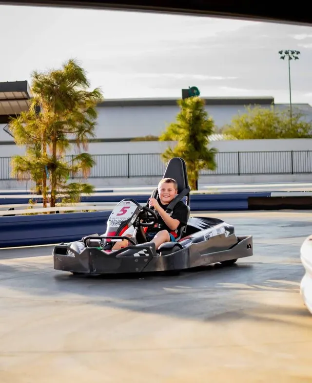 Person driving a black go-kart on an outdoor track, wearing a helmet and smiling.
