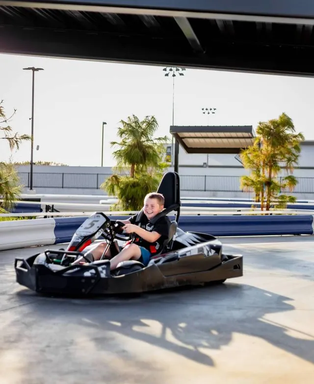 Person driving a black go-kart on an outdoor track in bright sunlight
