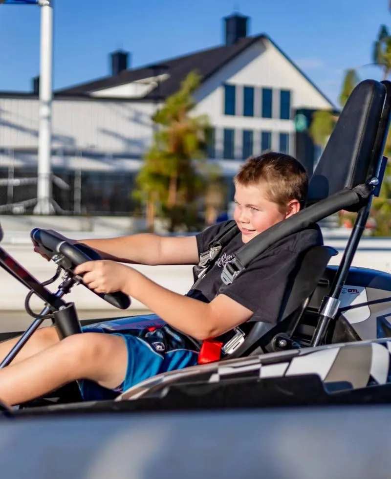 Boy driving a go-kart outdoors on a sunny day, with a house in the background