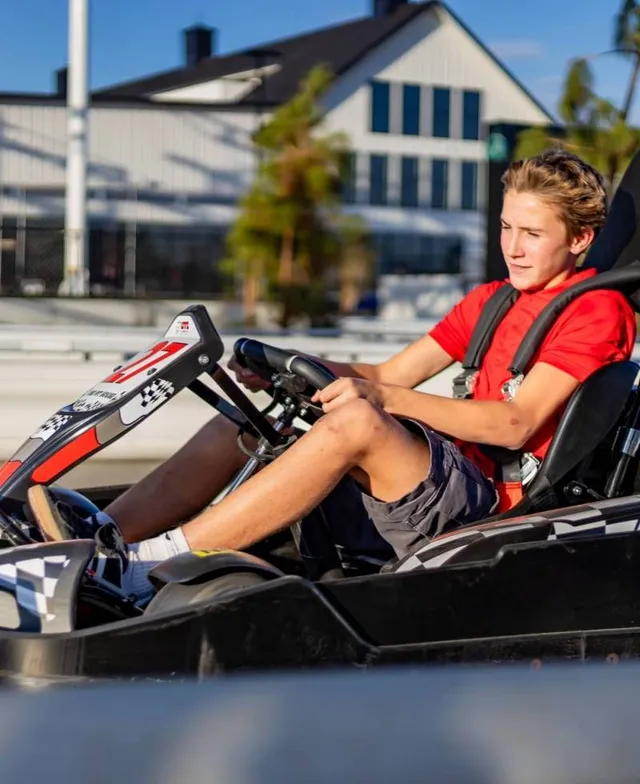 Person in a red shirt driving a go-kart outdoors near buildings.