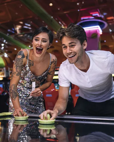 Two people smiling while playing a tabletop game in a bright arcade.