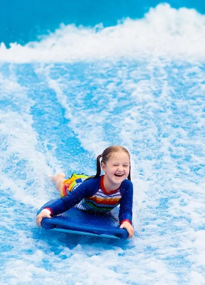 Smiling child sliding on a blue water slide, splashing through white water.